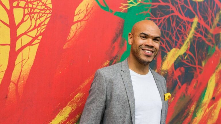 Man smiling before colorful mural background.