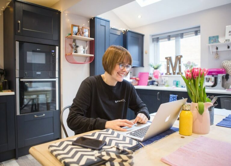 Woman working on laptop in modern kitchen.
