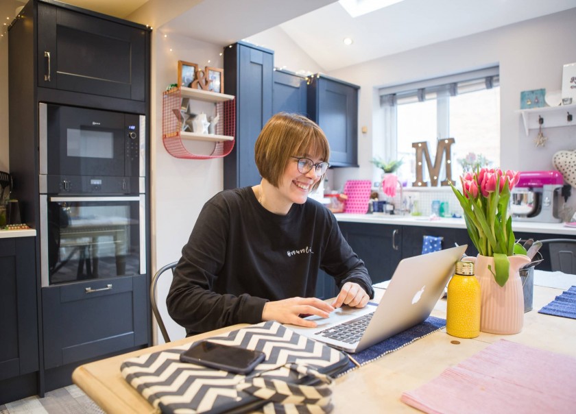 Woman working on laptop in modern kitchen.