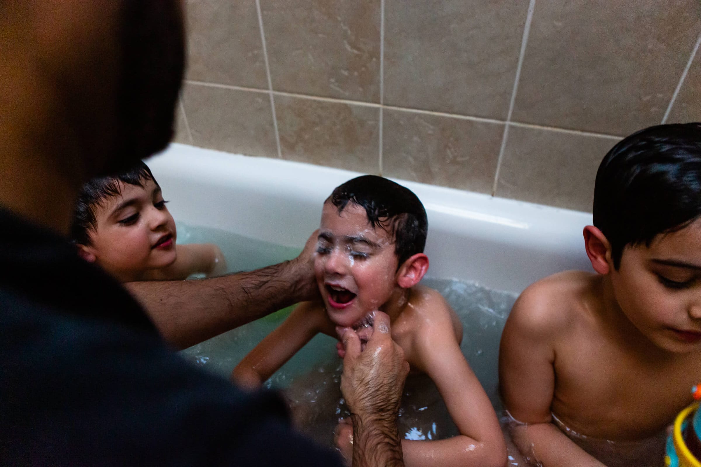 Three brothers in the bath and their Dad is washing the face of the middle boy | Documentary Family Photographer