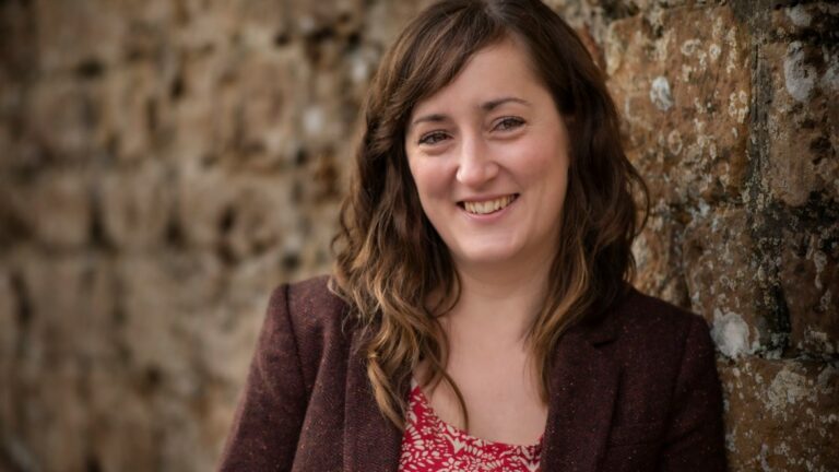 Woman smiling, stone wall background.