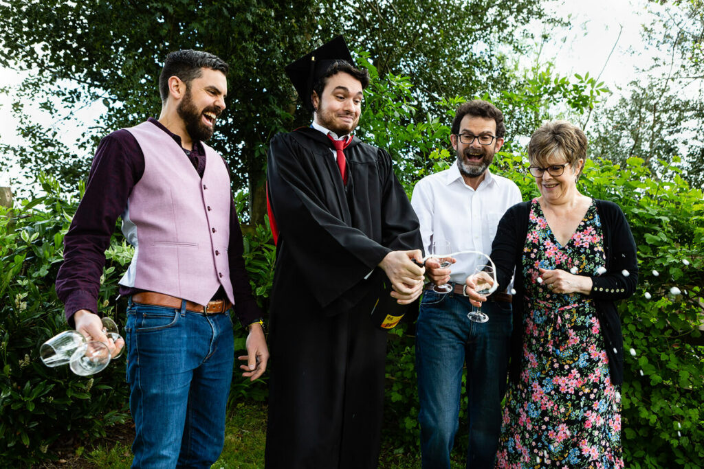 Graduate celebrating with family outdoors holding champagne glasses | Bath Bristol Graduation photographer | Rose Dedman