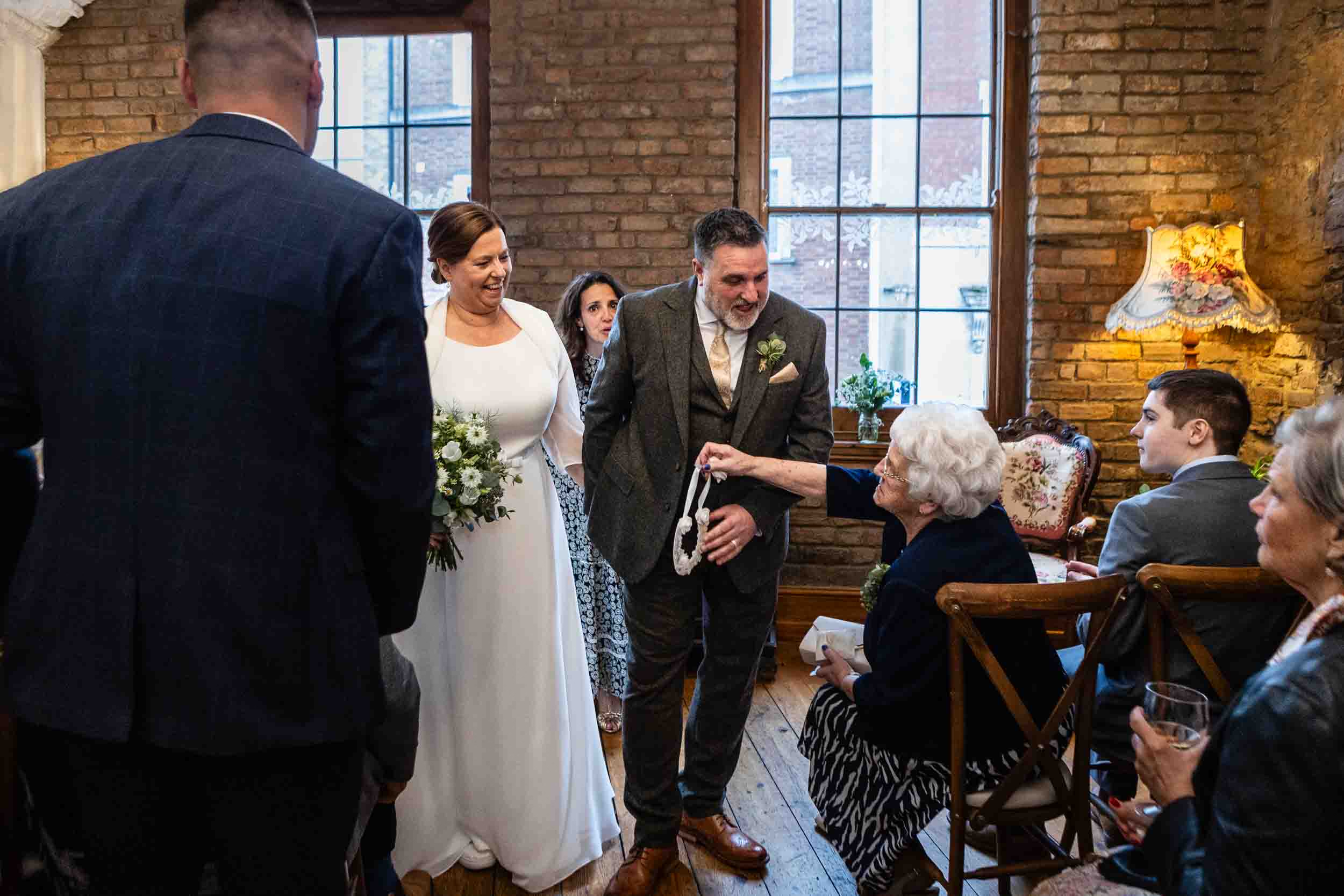 Older lady handing the bride and groom a lucky horse shoe as they walk back up the aisle at the Radnor Rooms wedding venue, Bristol.