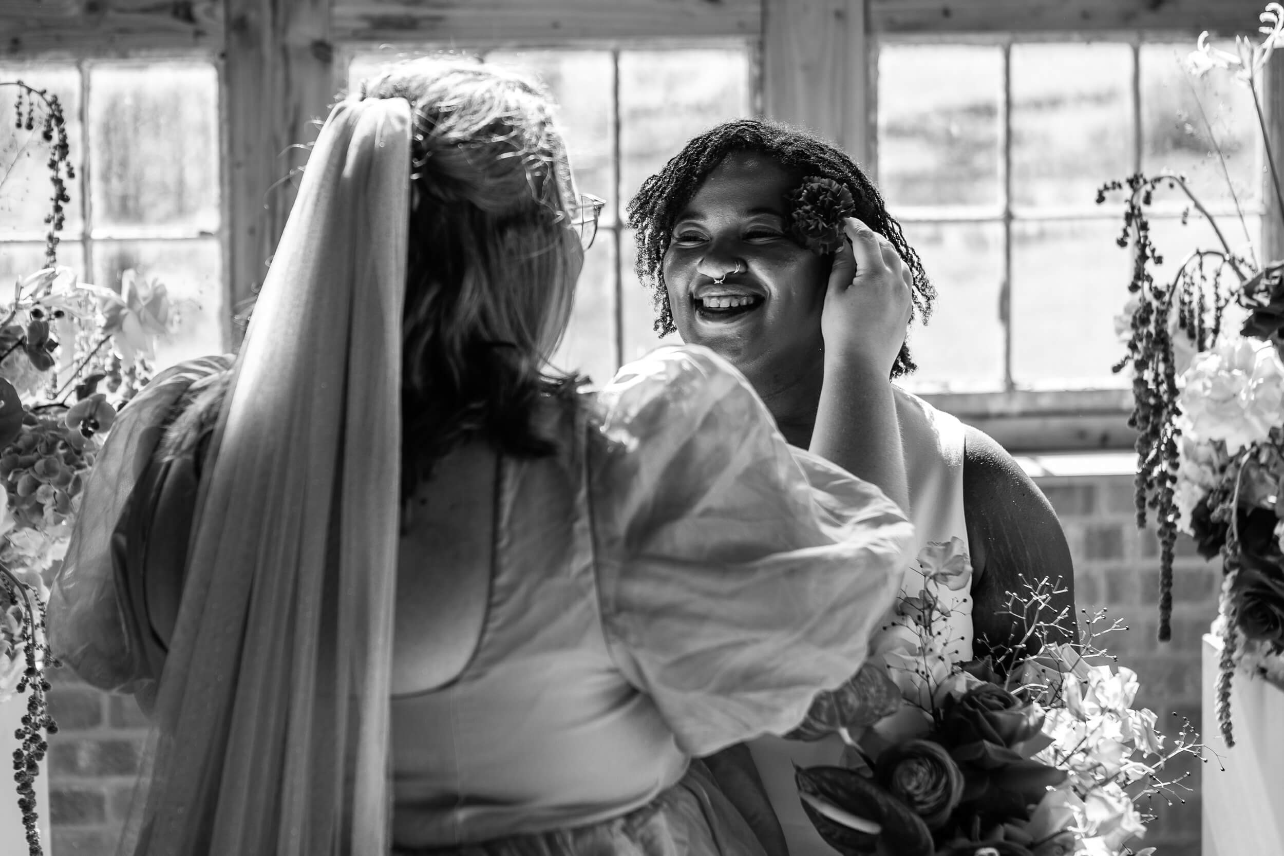 One bride putting a flower behind another bride's ear. LGBTQ+ wedding photographer Bristol, Bath and beyond.