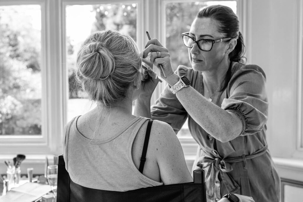 Makeup artist applies eyeliner to seated woman | Pennard House wedding photographer | Planning Your Wedding Photography at Pennard House