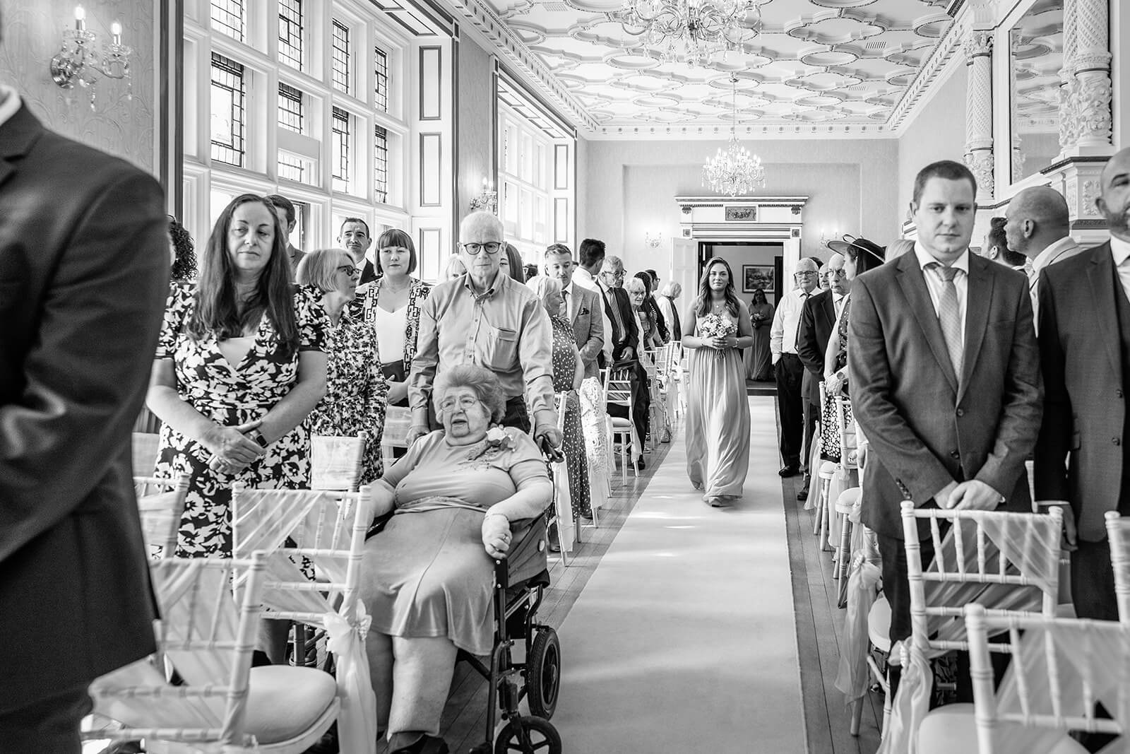 Wedding guests stand as bridesmaid walks down aisle at Holmewood Hall. Somerset wedding photographer.