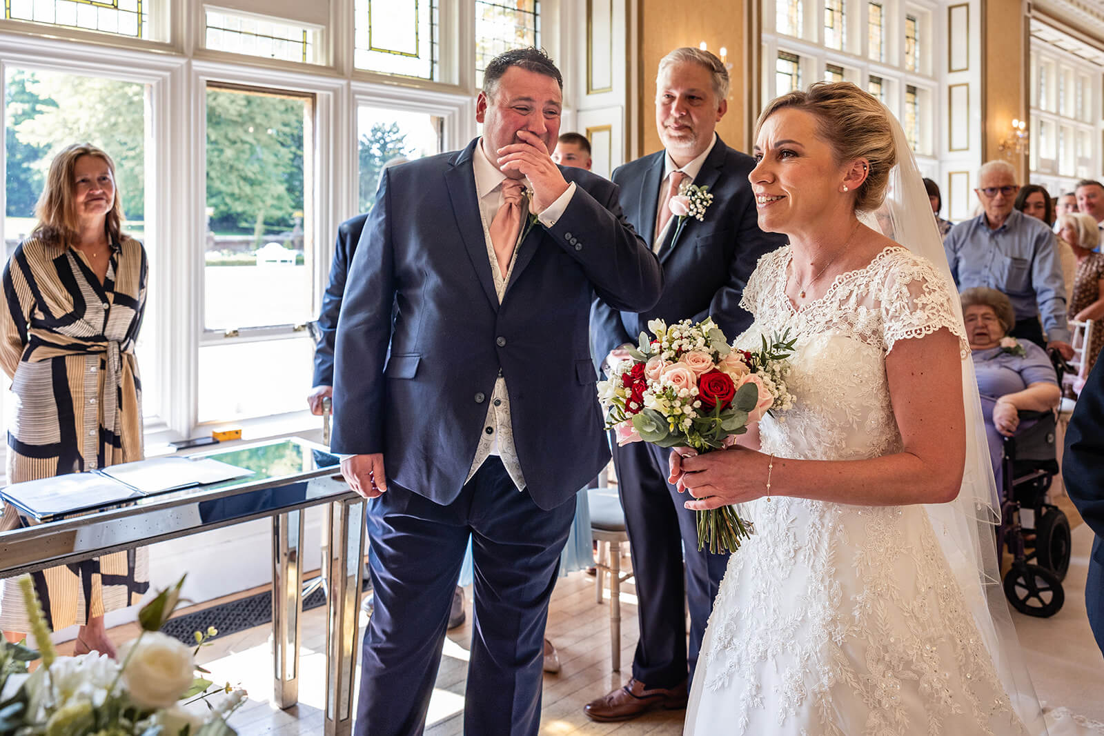 Bride walking down the aisle, smiling with bouquet at Holmewood Hall  country house wedding venue in Cambridgeshire UK (not in Somerset).