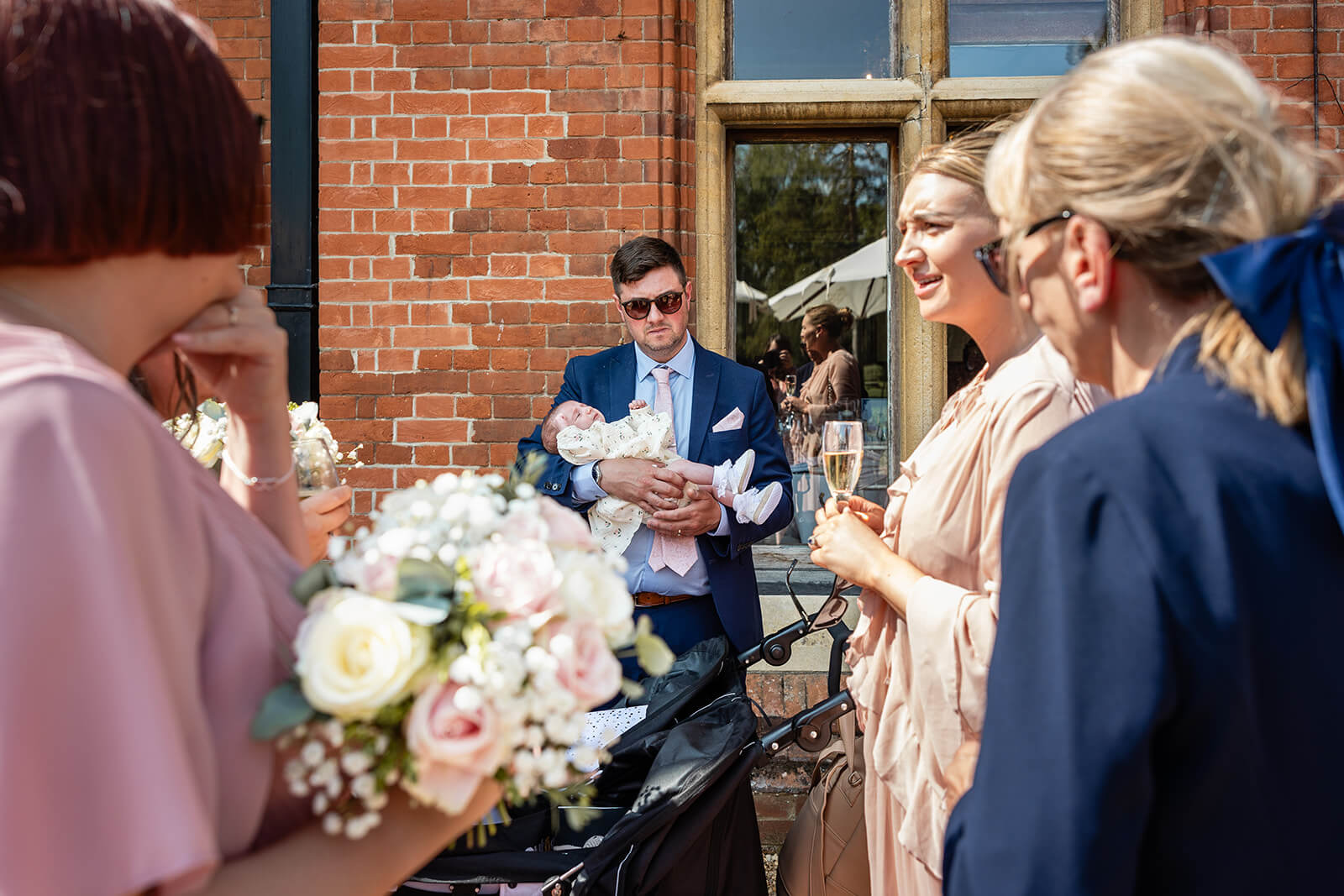 Group celebrating outside with baby and flowers at Holmewood Hall wedding.