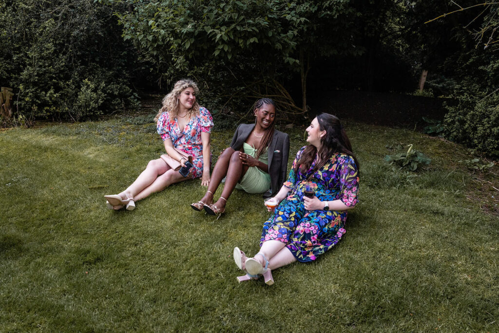 Three women chatting on lawn with drinks The Newt wedding photographer.