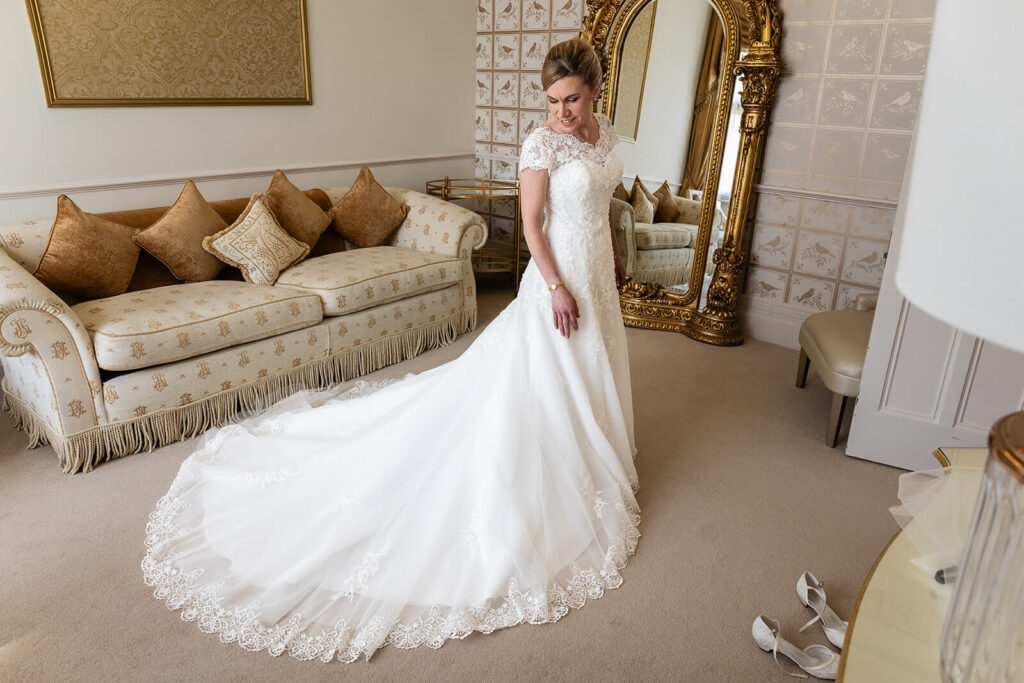Bride in white lace gown admiring dress. Cotswold wedding photographer