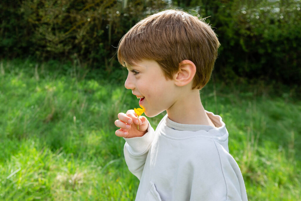 Child holding yellow flower in green field.