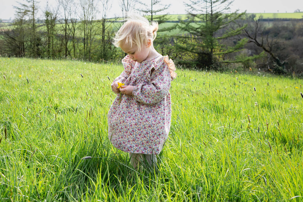 Child in field holding yellow flower, springtime scene.