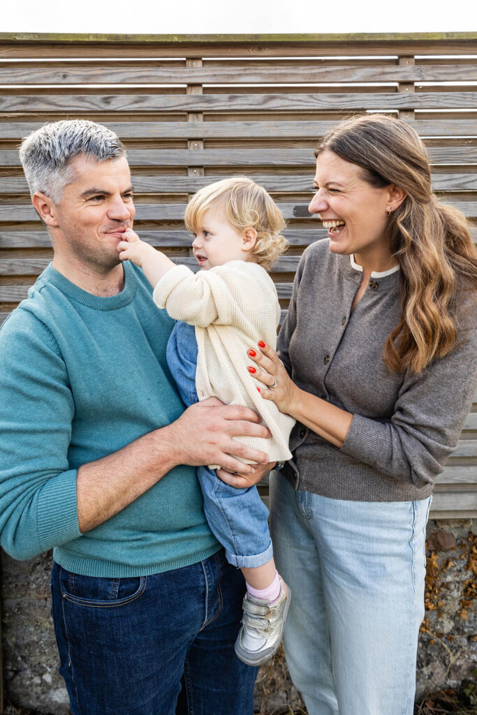 Family laughing outdoors, child in father's arms.
