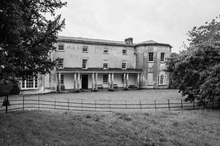 Historic country house with pillars and large trees.