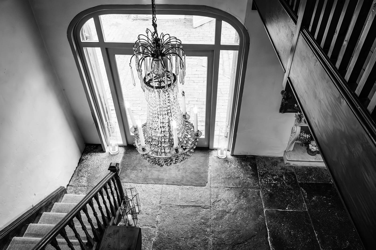 Elegant chandelier above stone staircase in entrance hall at Pennard House wedding venue. By Pennard House wedding photographer Rose Dedman.