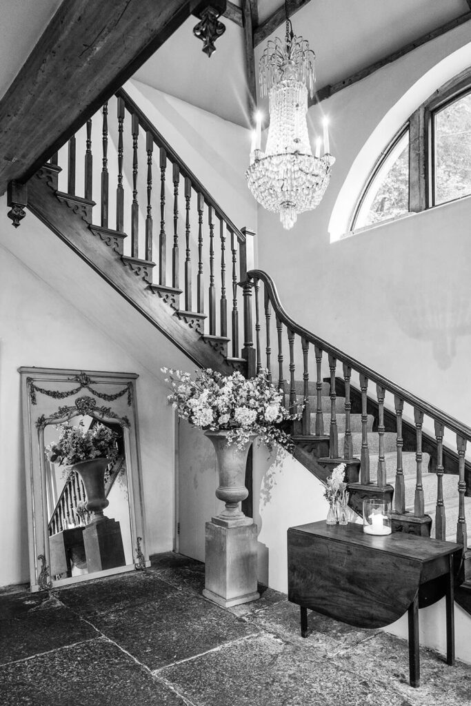 Elegant staircase with chandelier and floral arrangements, by Pennard House UK wedding photographer Rose Dedman.