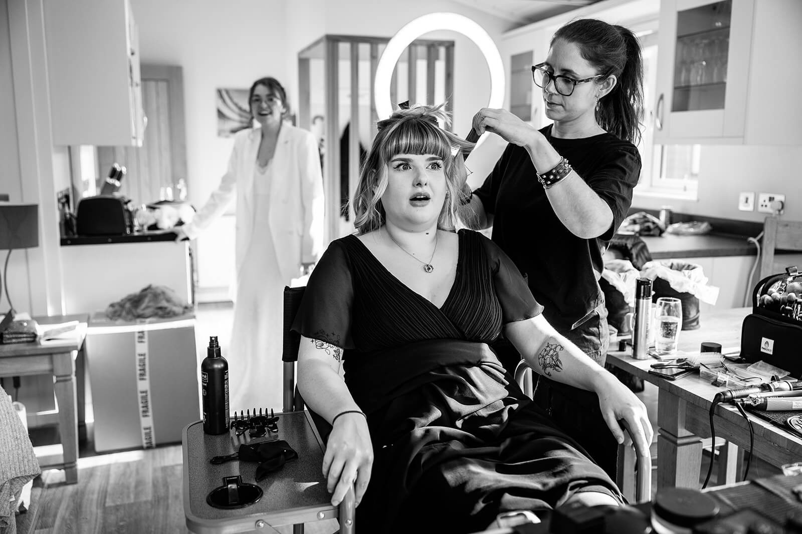 Woman getting hair styled with a funny expression, another woman smiling nearby.
