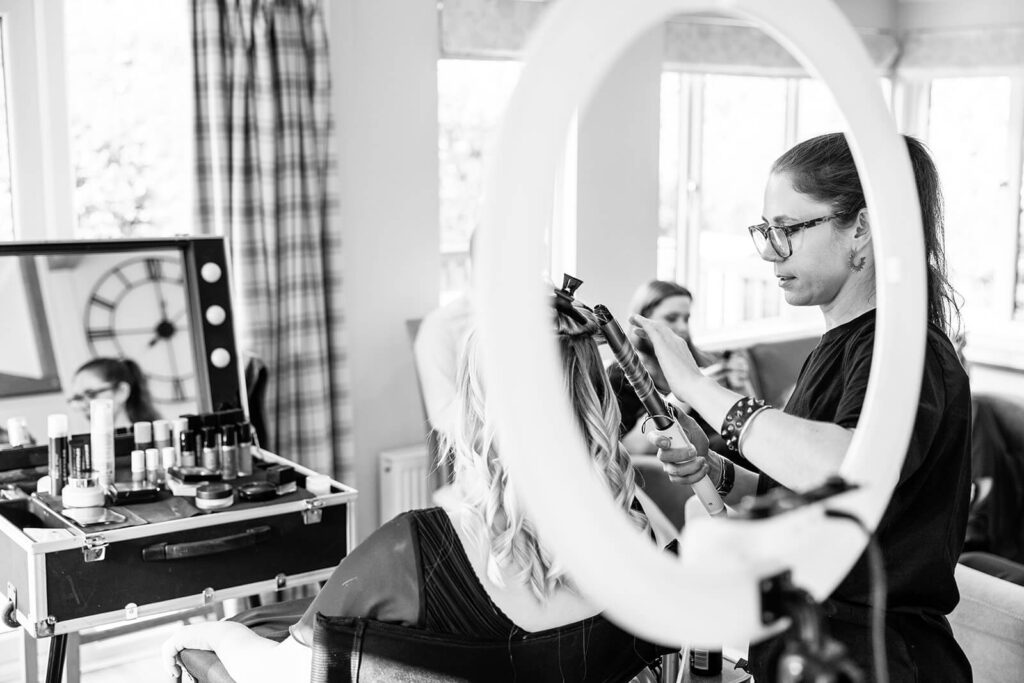 Hair stylist curling bridesmaid's hair during bridal prep at Bath Mill Lodges | Bath wedding photographer