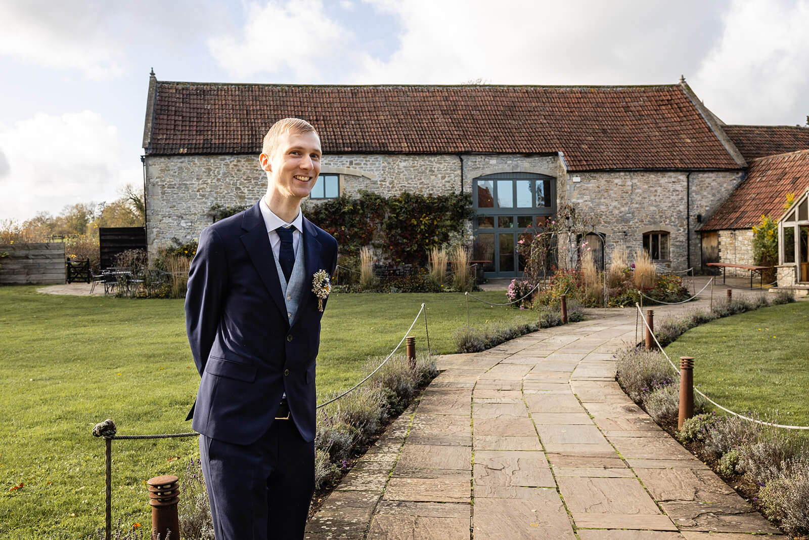 Groom in suit standing outside Priston Mill Tythe Barn ready to greet wedding guests | Priston Mill wedding photographer.