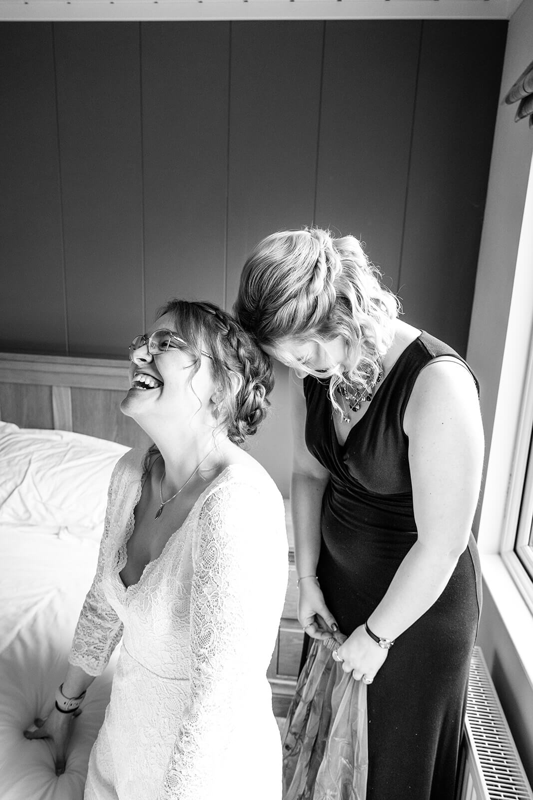 Bride and bridesmaid laughing together as they try to fit a veil to the bride during bridal prep at Bath Mill Lodges | Bath wedding photographer