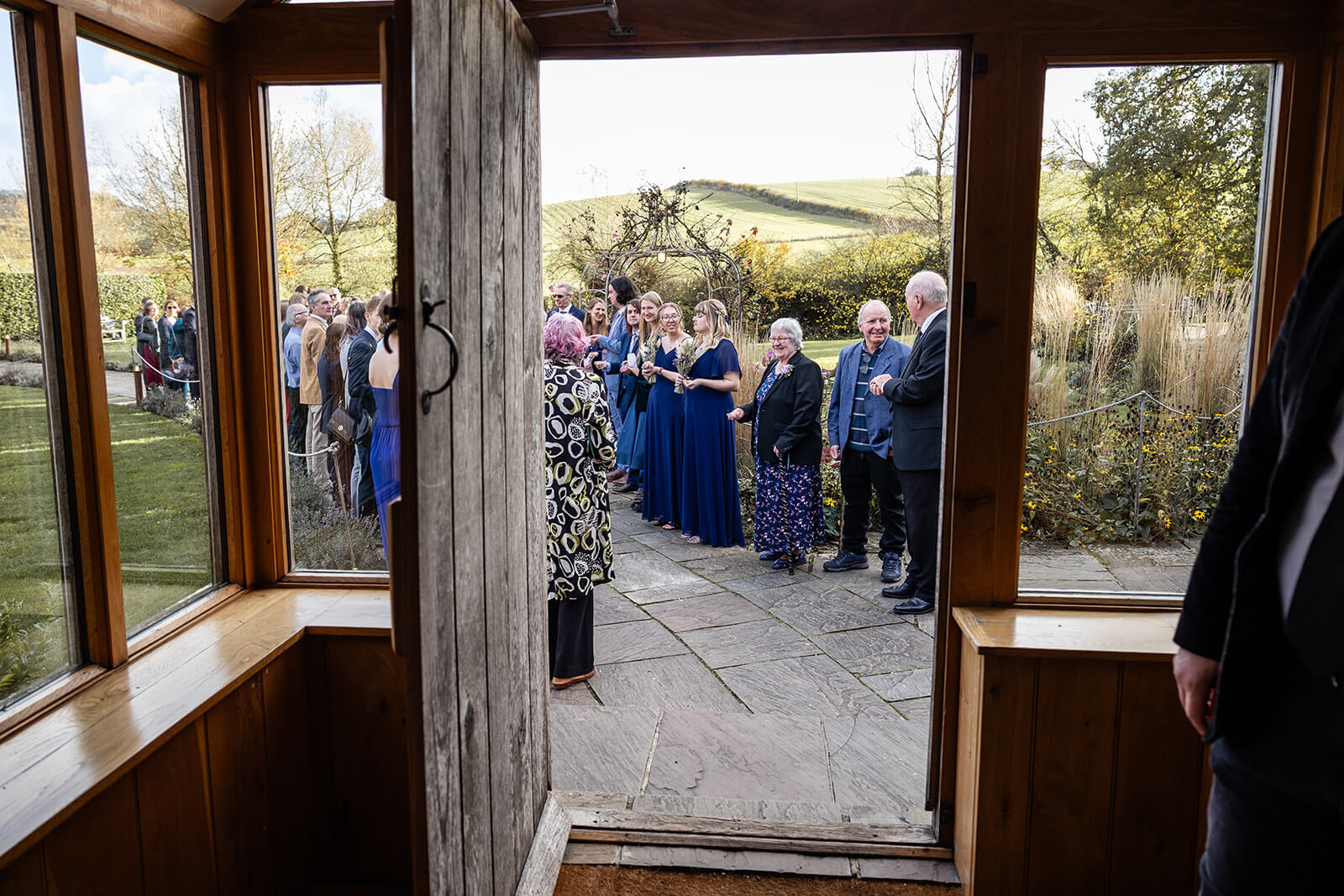Guests gather outside a wooden door ready for a confetti throw at a Priston Mill Tythe Barn wedding | Priston Mill wedding photographer.