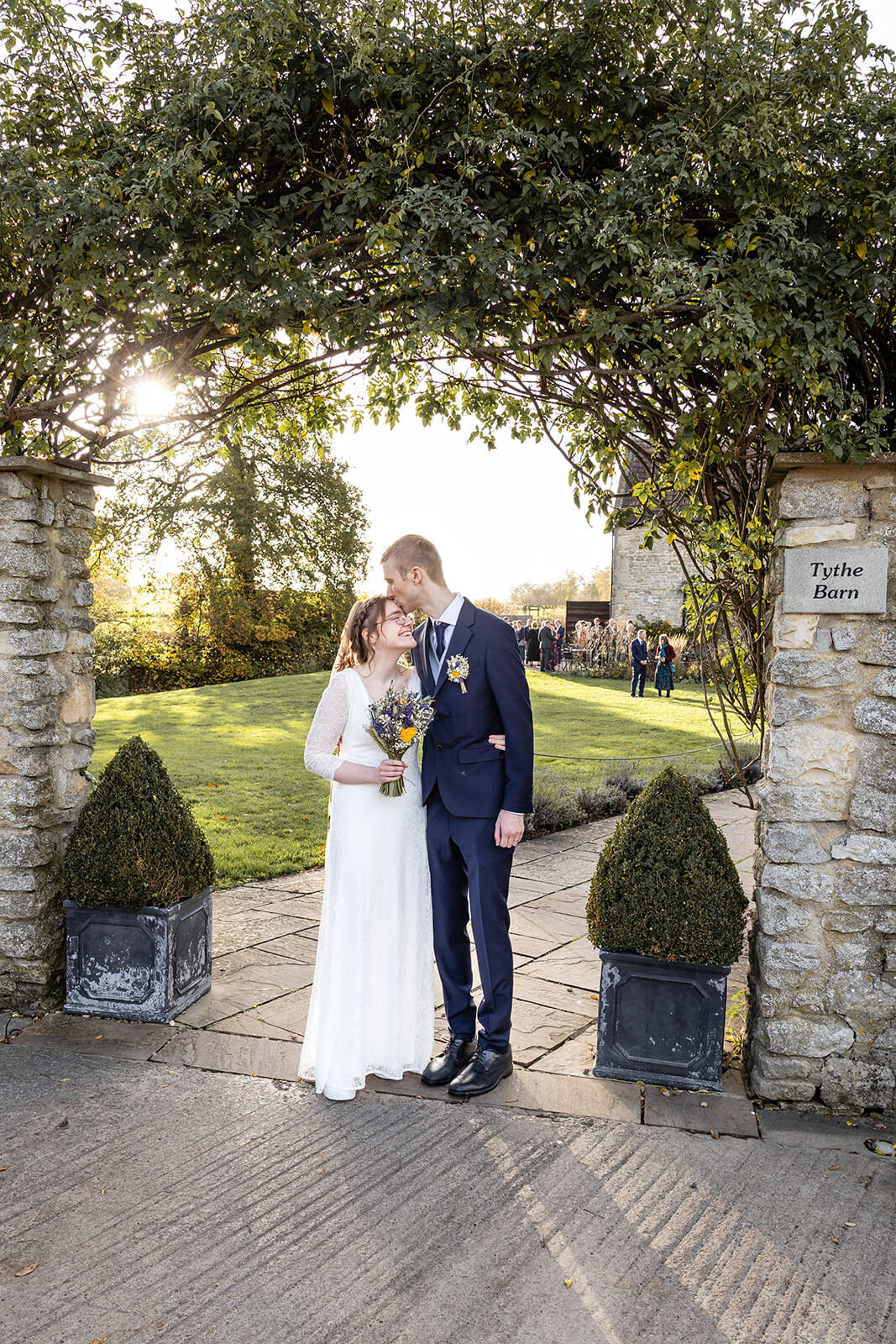 Newlyweds kissing in garden archway at Priston Mill's Tythe Barn | Priston Mill wedding photographer.