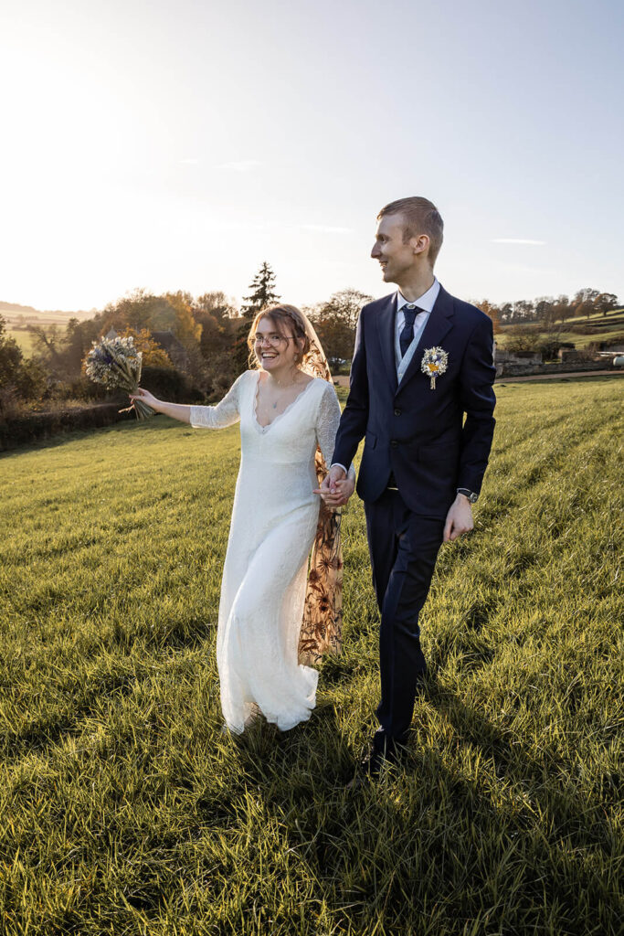 Happy couple walking in a field, during an autumn wedding day at Priston Mill. | Priston Mill wedding photographer.