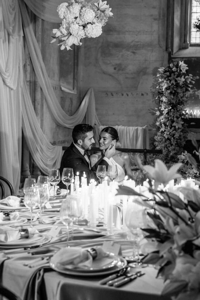 Bride at groom sat at table surrounded by candles and flowers in the Bell Tower of the Elvetham Estate. | Elvetham Estate wedding photographer.