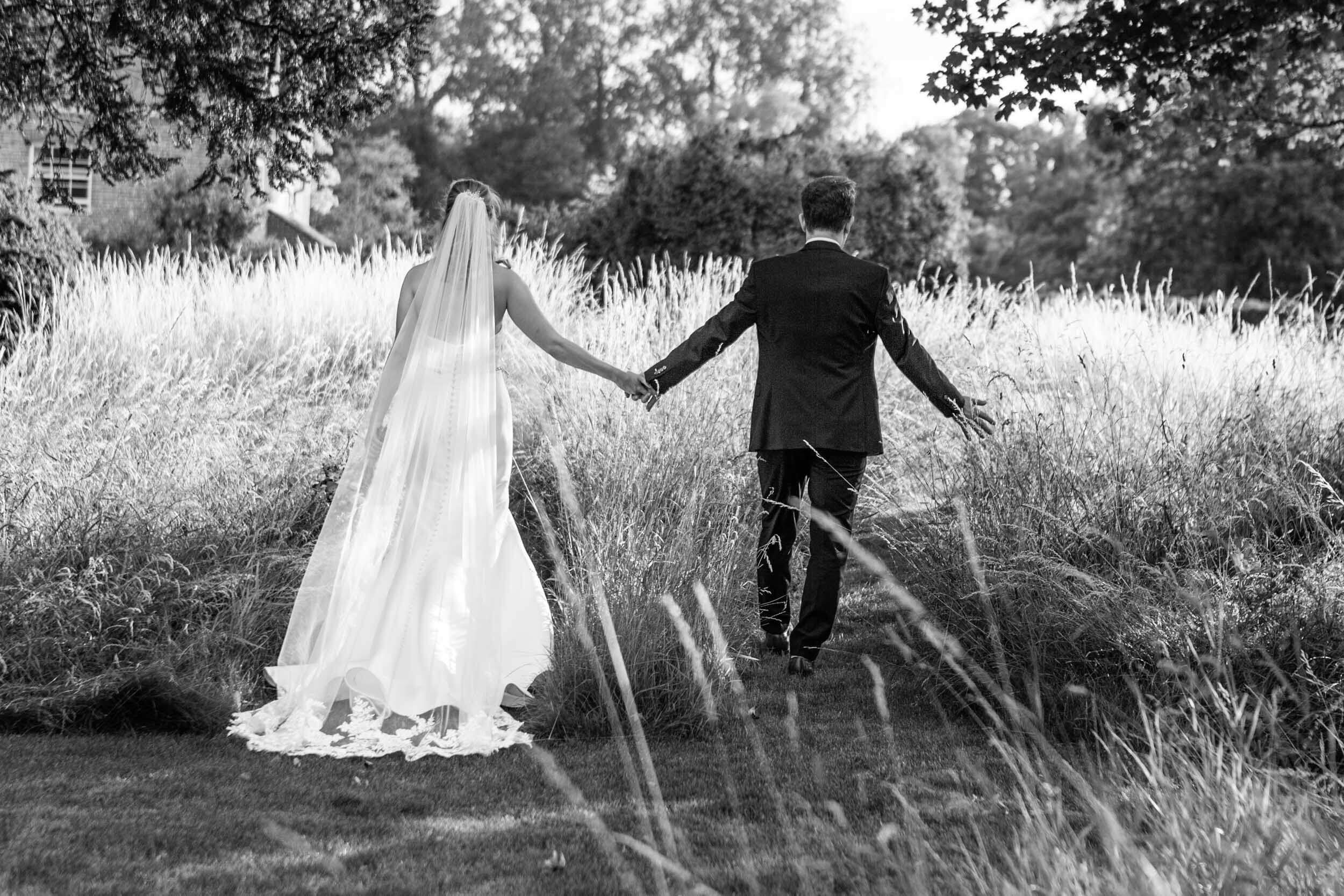 View of bride and groom from behind, holding hands in garden at Syrencot House.
