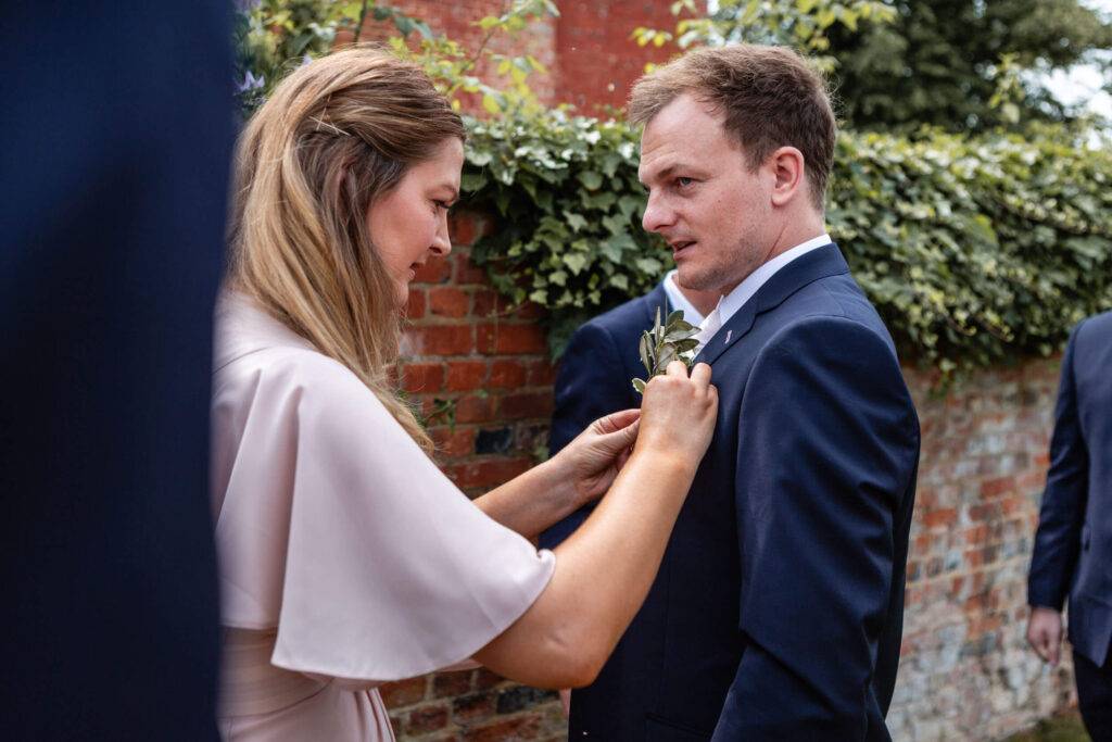 Woman adjusting boutonnière on man's suit jacket.