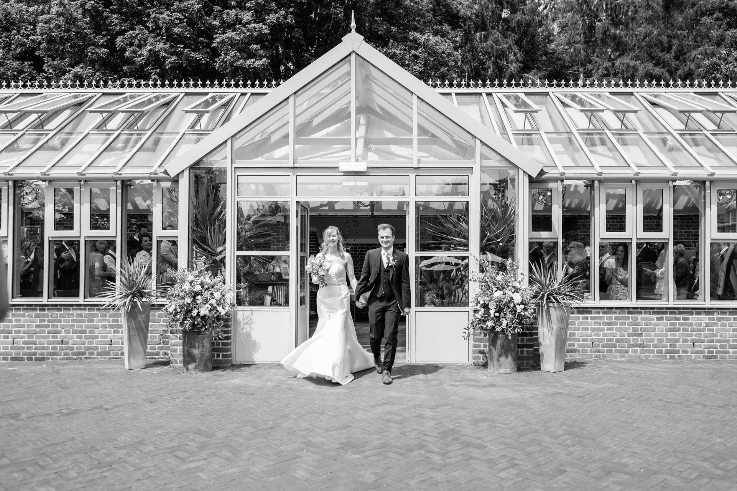 Bride and groom exit glass building on wedding day at Syrencot.