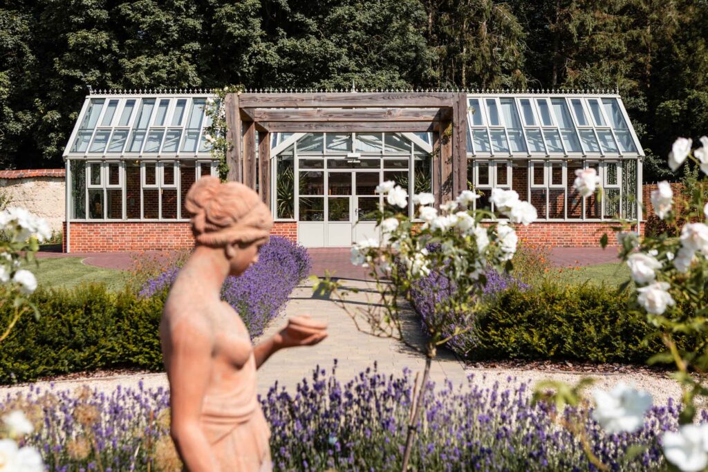 Garden statue, flowers, and greenhouse in background.