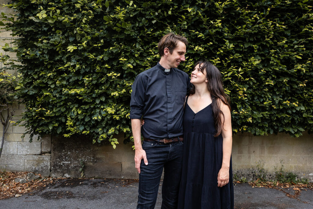 Couple standing against leafy wall.