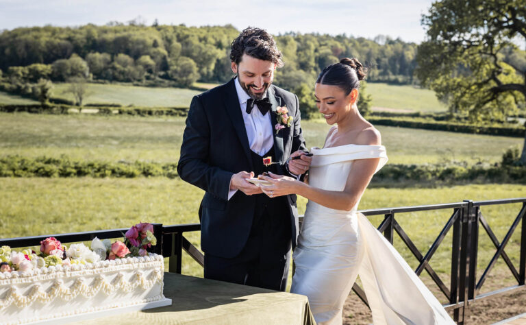 Bride and groom cutting wedding cake outdoors.