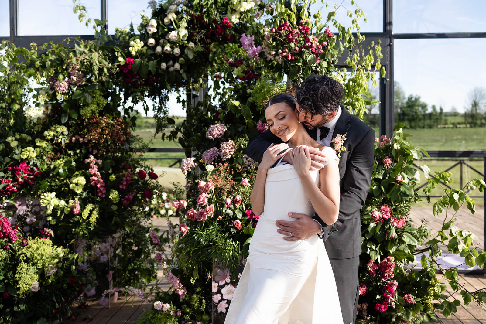 Couple embracing in front of floral arch.